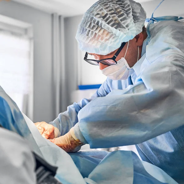手術室で腹部整形手術やおなかタック手術を行う眼鏡の男性の整形外科医 腹部の整形手術をしながら外科的制服と医療面マスクを身に着けている男医師 — ストック写真