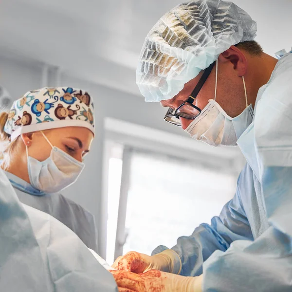 Doctors performing abdominoplasty surgery in clinic. Male plastic surgeon and female assistant conducting abdominal plastic surgery in operating room. Concept of medicine, tummy tuck, cosmetic surgery