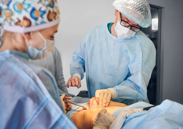 Plastic surgeon and assistant performing plastical surgical operation in hospital, removing excess fat from patient abdomen in operating room. Concept of medicine, abdominoplasty and aesthetic surgery