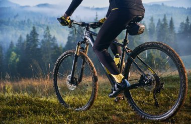 Çimenli tepede bisiklet süren bisikletli adam görüntüsü. Bulanık arkaplanda görkemli dağların manzarası. Spor, bisiklet ve doğa kavramı.