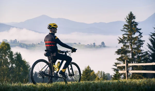 骑自行车骑自行车站在长满青草的山上 望着美丽的薄雾的群山 骑自行车的男性骑自行车的人喜欢观赏雄伟的高山 自行车 自然的概念 — 图库照片