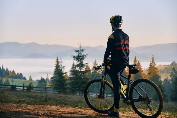 早上骑自行车的男性骑手站在自行车旁边的倒影 骑自行车的人戴着安全帽在山上骑自行车 骑单车和积极休闲的概念 — 图库照片