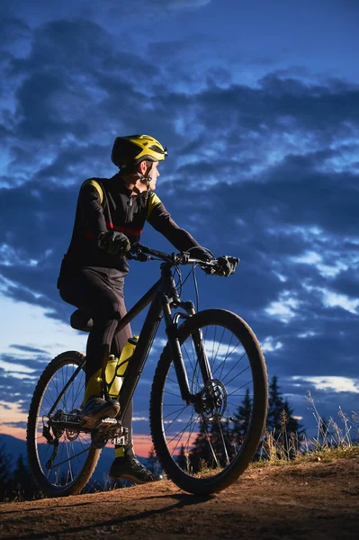 年轻人在美丽的夜空下骑自行车 晚上骑自行车时 骑自行车的男性骑自行车者在蓝色阴天下的山坡上休息 骑单车和积极休闲的概念 — 图库照片