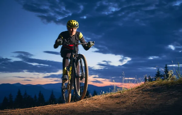 黄昏的时候 年轻的骑车人骑着自行车在山上晃来晃去 骑自行车的人戴着头盔 穿着制服在野外旅行 水平快照 极端体育运动的概念 — 图库照片