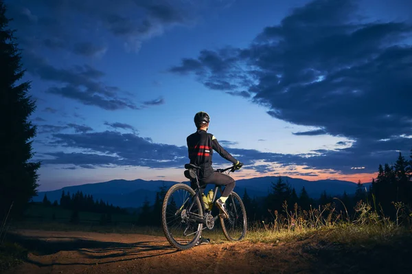 在乌云笼罩的蓝色夜空下 人们骑自行车的背景图 晚上骑自行车的男性骑自行车的人戴着安全帽在小径上骑车 骑单车和积极休闲的概念 — 图库照片