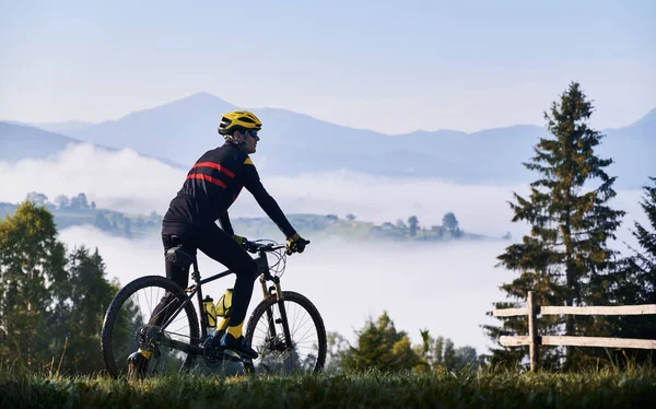 骑自行车的骑自行车的人在青草山上的轮廓 骑自行车的男性骑自行车的人喜欢观赏雄伟的高山 自行车和自然的概念 — 图库照片