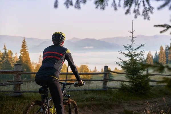 从后面看骑自行车 背山的男性骑手 骑自行车的人戴着安全帽在山上骑自行车 积极休闲的概念 — 图库照片