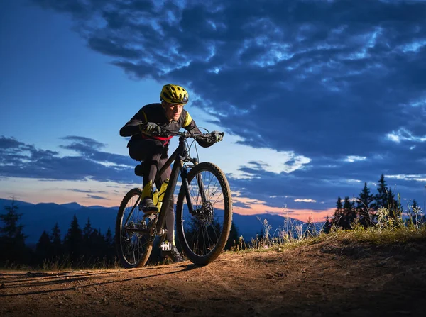 在美丽的夜空下骑自行车的年轻人的背景图 傍晚时分 骑着安全帽骑在蓝色阴天下山坡路上的男性骑自行车者 体育与积极休闲的概念 — 图库照片