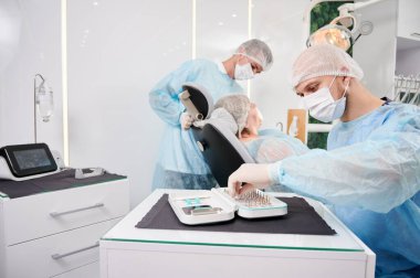 Erkek dişçi diş implantlarını seçiyor, dişçi koltuğunda kadın yatarken diş implant setiyle masada oturuyor. Diş sağlığı, stomatoloji ve diş bakımı kavramı.