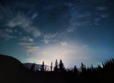 Bulutlar, güzel ağaçlar ve doğa ile inanılmaz mavi gökyüzü. Mavi gökyüzü altında kozalaklı dağ ormanlarının manzarası yıldızlar ve kuyruklu yıldız Neowise.