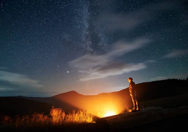 Unge Man Står Stockar Nära Lägerelden Bergen Himlen Full Stjärnor — Stockfoto