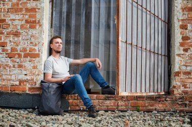 Sırt çantası tuğla kaplı gülümseyen genç adamın ön görüntüsü. Şehrin dışındaki temiz havada dinlenme kavramı..