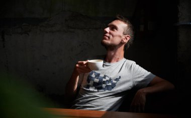 Yakından, rahat bir sandalyede oturan, elinde fincan kahve içen genç bir adam. Sıcak içecekle boş zaman geçirme kavramı.