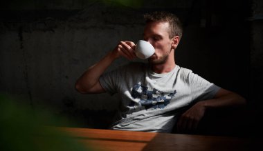 Kafede bir fincan kahveyle dinlenen bir erkek. Genç adam masada oturup kahve içiyor. Kafede dinlenme kavramı.