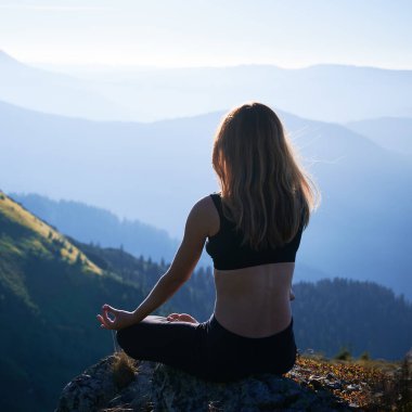Esmer kadının Lotus pozunda yoga çalışmasını. Spor giyimli bir kadın dağlardaki çimenler üzerinde meditasyon yapıyor. Formda vücut kavramı.
