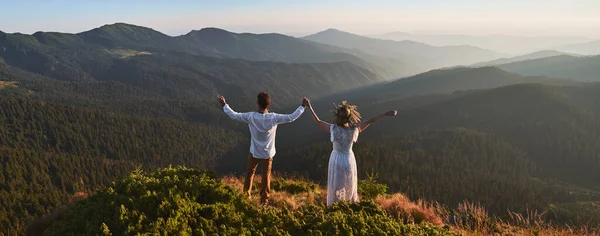 白い服を着た幸せなカップルのバックビューの山の上に立っている 女とボーイフレンドの手と山の称賛を保持している 美しい風景の概念 — ストック写真