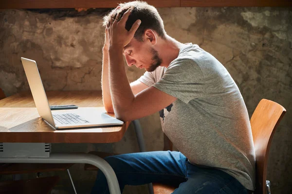 Side view of irritated and pensive young man working or studying in laptop. Concept of thinking about working in home.