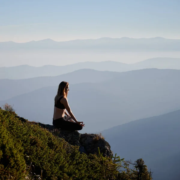 ロータスポーズでヨガを練習する女性のサイドビュー 瞑想の女性は山の中で草の上でリラックスしている 自然との調和の概念 — ストック写真