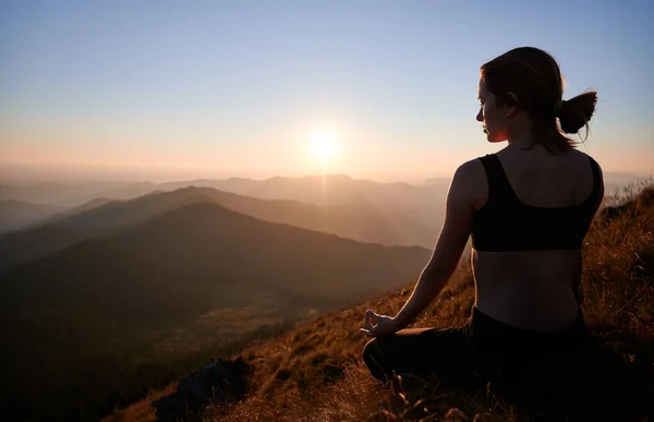 女性は夜に山の中でロータスポーズでヨガを練習 瞑想の女性は芝生の上でリラックスして夕日を見ています 自然との調和の概念 — ストック写真