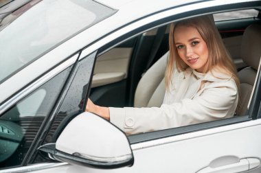 Modern araba kullanan güzel genç bir kadın. Kadın sürücü arabada oturuyor ve kameraya gülümsüyor..