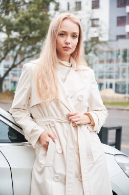 Modern beyaz arabasının yanında poz veren güzel genç bir kadının portresi..