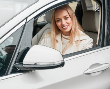 Güzel, gülümseyen sarışın bir kadının portresi. Direksiyonun başında oturuyor. Mutlu bayan rahat beyaz arabasında sürücü koltuğunda dinleniyor..