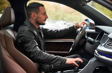 Arabanın içinde yan görüş. Rahat modern otomobilini kullanan çekici çocuk. Otomobil sürücüsü dikkatle yola bakıyor, bir elini direksiyona, diğerini vites kutusuna koyuyor..