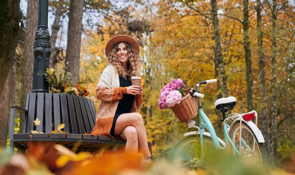 아름다운 여자가 뒤쪽으로 자전거를 커피를 마시고 벤치에 이보입니다 정어리 은가을 — 스톡 사진