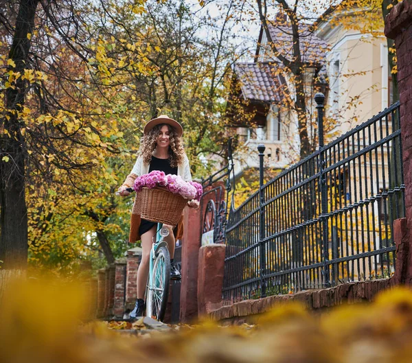 모자를 자전거를 고대의 울타리 나무등을 배경으로우아 역파란 자전거를 곱슬머리의 소녀의 — 스톡 사진