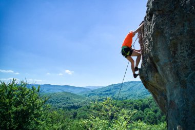Erkek kaya tırmanıcısının engebeli kireçtaşı kayalıklara tırmanırken güvenlik için koşum takımı ve ip ile hava görüntüsü. Sporcu Ukrayna 'nın Karpatya dağlarındaki Dobvush Kayaları' nda dikey büyük kaya parçasına tırmanıyor.