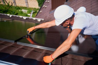 Evin çatısına güneş paneli inşa eden bir işçi. Dışarıda fotovoltaik güneş modülü kuran miğferli ve eldivenli adam mühendisi. Alternatif, yeşil ve yenilenebilir enerji üretimi kavramı.