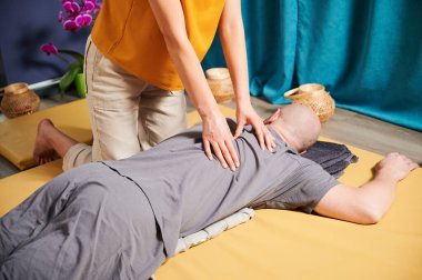 Masör Tayland yogası masajı yapıyor. Kadın terapistin erkek hastalara evde geleneksel masaj uygulaması. Kel müşteri meditasyon yapıyor, sakin atmosferde el masajının keyfini çıkarıyor..