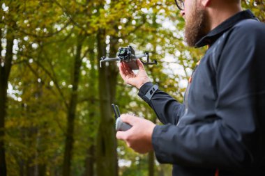 Altın yapraklarla dolu canlı bir ormanda, bir insan bir dronu ustalıkla yönetir, doğanın güzelliğinin tadını çıkarırken, çevrenin çarpıcı hava görüntülerini yakalar..