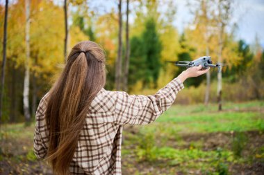 Genç bir insan, sonbahar boyunca canlı bir ormanda duruyor ve renkli ağaçlara ve doğaya bir dron fırlatmaya hazır. Sahne huzurlu ve hayat dolu..