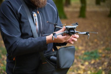 Sonbahar aylarında sakin bir ormanda bir adam, düşen yapraklar ve yüksek ağaçların arasında uçmaya hazırlanan bir dronu dikkatle tutar..