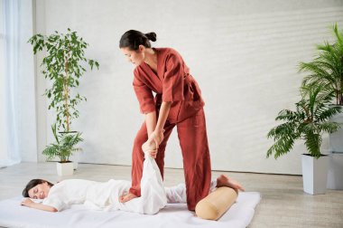 Masör Tayland yogası masajı yapıyor. Kadın terapist, kadın hasta için evde geleneksel masaj tedavisi uyguluyor. Müşteri paspasın üzerinde uzanıyor, meditasyon yapıyor, sakin bir atmosferde el masajının keyfini çıkarıyor..