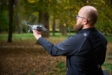 İnsansız hava aracı meraklısı, sonbahar yaprakları düşerken uçmaya hazır ağaçlarla çevrili yemyeşil bir parkta duruyor. Yumuşak akşam ışığı anı güçlendirir..