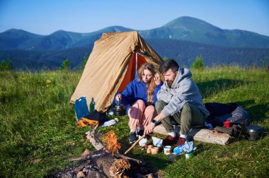 Sabahları iki çadırı olan manzaralı dağ kampı. İki kampçı, bulutsuz gökyüzünün altında yuvarlanan dağların huzurlu manzarasının keyfini çıkarıyorlar. Resimli gündoğumu manzarası, huzurlu ve rahat bir açık hava deneyimi yaratıyor..