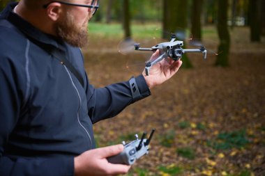 Huzurlu bir ormanda bir elinde insansız hava aracı diğer elinde uzaktan kumandayla duran bir adam..