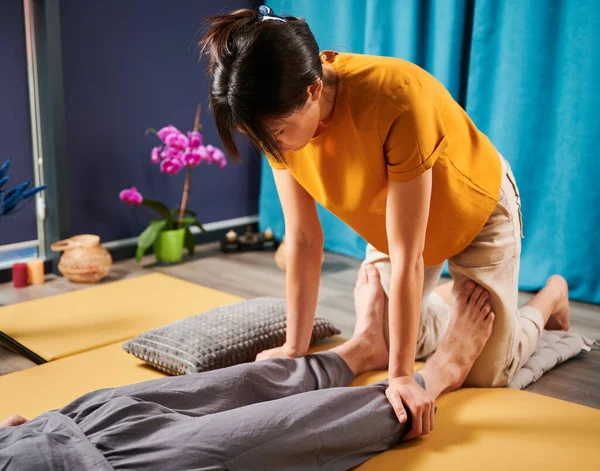 Masör Tayland yogası masajı yapıyor. Kadın terapist erkek hasta için evde geleneksel masaj tedavisi uyguluyor. Müşteri paspasın üzerinde uzanıyor, meditasyon yapıyor, sakin bir atmosferde el masajının keyfini çıkarıyor..