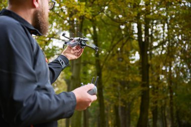 Rengarenk bir ormanda elinde uzaktan kumandalı bir dronla duran bir adam sonbaharın altın yaprakları arasında uçmaya hazır, doğanın güzelliğinin tadını çıkarıyor..