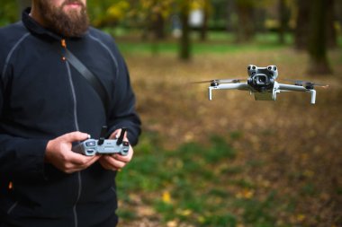 Odaklanmış bir adam huzurlu sonbahar parkında süzülen bir dronu kontrol eder. Renkli yapraklar ve doğal güzelliklerle çevrili..