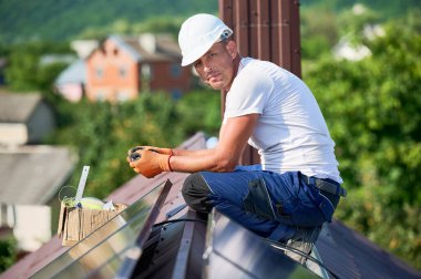 Evin metal çatısında güneş paneli inşa eden bir işçi. Dışarıda fotovoltaik güneş modülü kuran mühendisin portresi. Alternatif, yeşil ve yenilenebilir enerji üretimi kavramı.