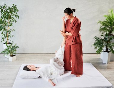 Masör Tayland yogası masajı yapıyor. Kadın terapist, kadın hasta için dirsek kullanarak geleneksel masaj tedavisi uyguluyor. Müşteri paspasın üzerinde uzanıyor, meditasyon yapıyor, sakin bir atmosferde el masajının keyfini çıkarıyor..