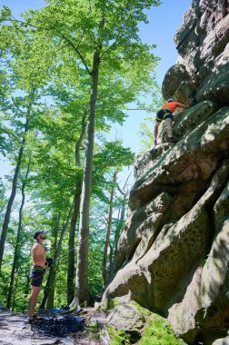 Erkek kaya tırmanışçısı güvenlik için kayış takımı ve iple engebeli kireçtaşı uçurumuna tırmanıyor. Sporcu Ukrayna 'nın Karpatya dağlarındaki Dobvush Kayaları' nda dikey büyük kaya parçasına tırmanıyor.