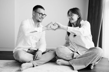 Genç baba ve kızı elleriyle kalp sembolü yapıyorlar. Aileyle vakit geçirmek güzeldi. Çocukla babanın birbirlerine sevgilerini gösterdikleri tatlı bir an. Siyah ve beyaz resim.