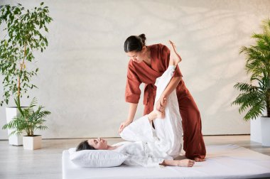 Masör Tayland yogası masajı yapıyor. Geleneksel masaj tedavisi uygulayan kadın terapist, kadın hastaların vücudunu geriyor. Müşteri paspasın üzerinde uzanıyor, sakin atmosferde el masajının keyfini çıkarıyor..