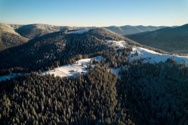 Karla kaplı tarlalar ve yoğun çam ormanlarıyla nefes kesici kış manzarası. Ağaçların arasına kurulmuş küçük bir köy. Uzak dağlar görkemli bir şekilde masmavi gökyüzünün altında duruyor..