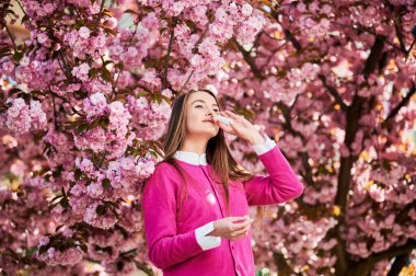 Burun spreyi kullanan alerjik bir kadın baharda çiçek açan bahçede mevsimsel alerjiden muzdarip. Açık havada çiçek açan ağacın önünde akan burnu tedavi eden genç bir kadın. Bahar alerjisi konsepti.