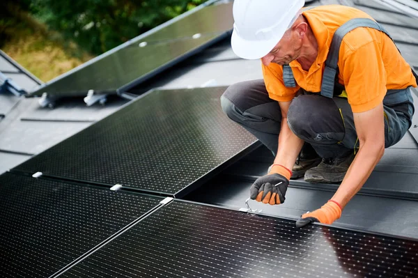 Evin çatısında fotovoltaik güneş paneli inşa eden bir işçi. Miğferlerde mühendis ve eldivenler dışarıda altıgen anahtarla güneş modülü kuruyor. Alternatif enerji üretimi kavramı.